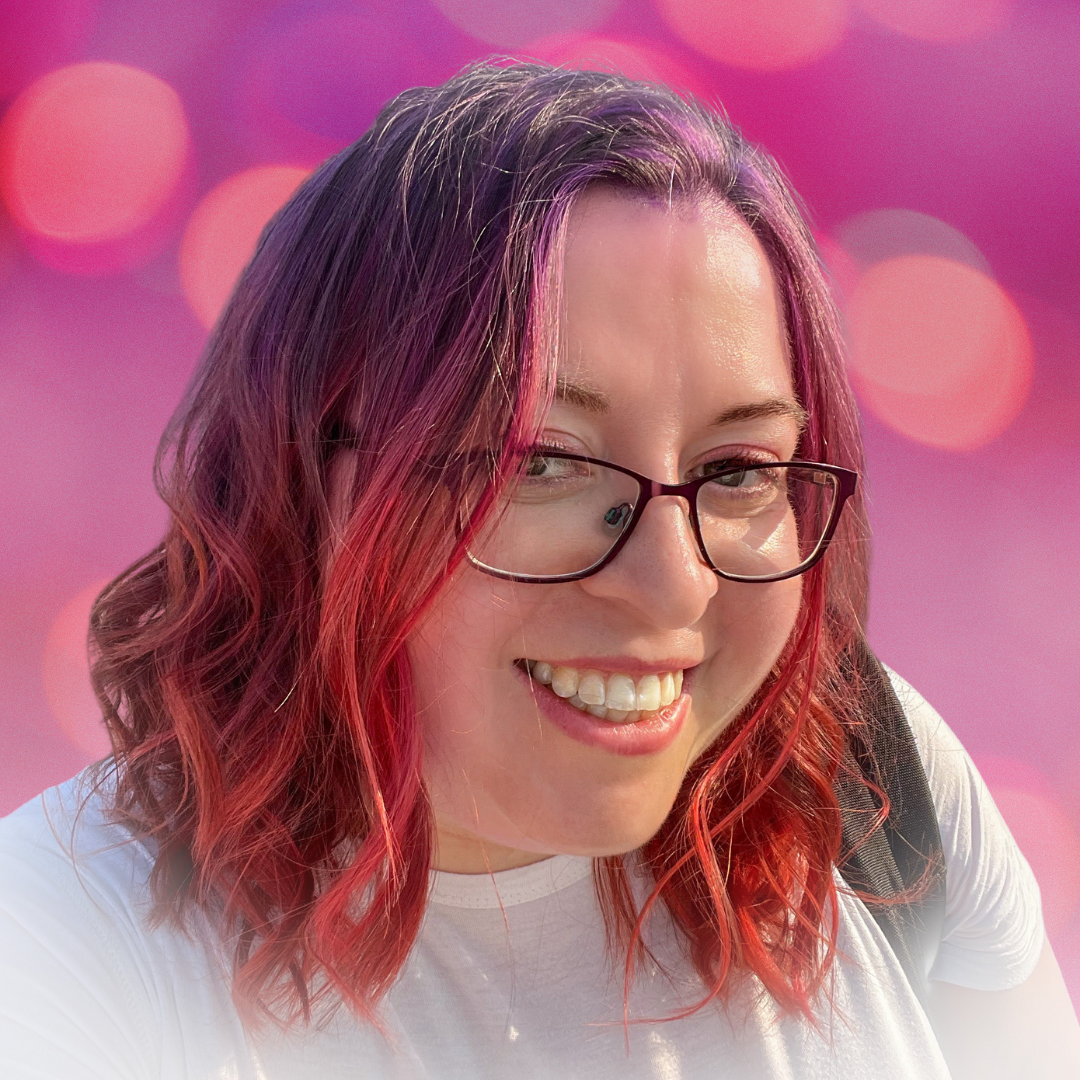 A smiling woman (Dani) with wavy hair dyed pink and purple, wearing glasses and a white shirt, against a soft pink background.
